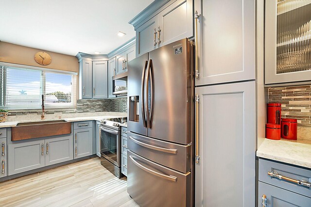 kitchen featuring decorative backsplash, appliances with stainless steel finishes, light stone countertops, sink, and light hardwood / wood-style floors