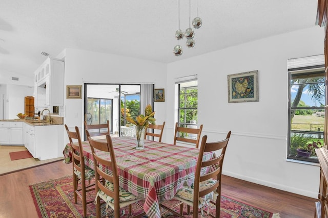 dining area with sink, wood-type flooring, and vaulted ceiling