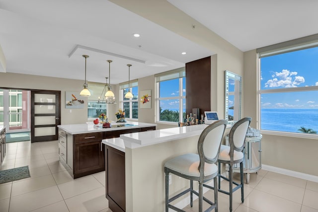 kitchen featuring dark brown cabinetry, light tile patterned floors, decorative light fixtures, a water view, and a center island