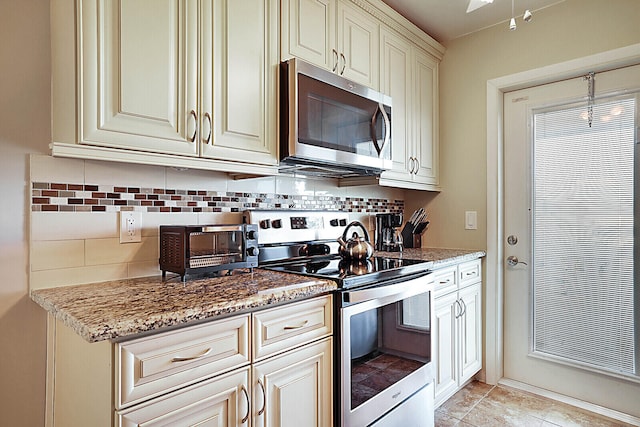 kitchen with appliances with stainless steel finishes, backsplash, stone counters, cream cabinetry, and light tile patterned flooring