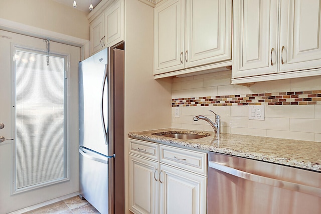 kitchen with light stone countertops, sink, backsplash, cream cabinets, and appliances with stainless steel finishes