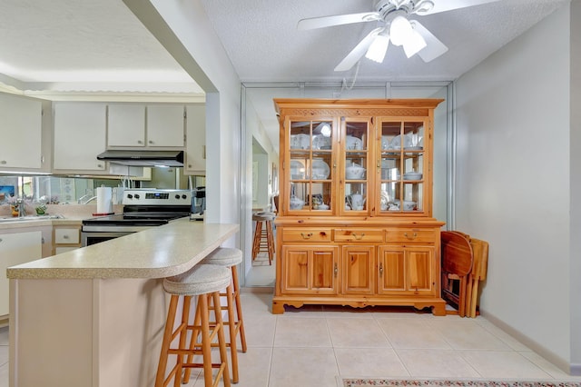 kitchen with light tile patterned flooring, a breakfast bar, stainless steel electric range oven, a textured ceiling, and kitchen peninsula