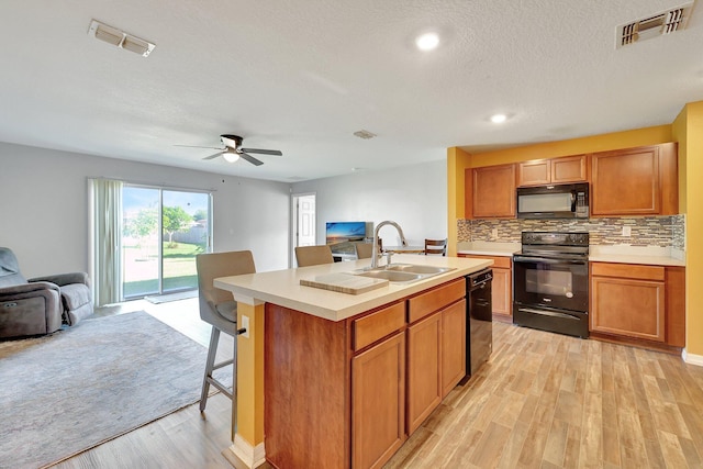 kitchen featuring ceiling fan, sink, black appliances, light hardwood / wood-style flooring, and an island with sink