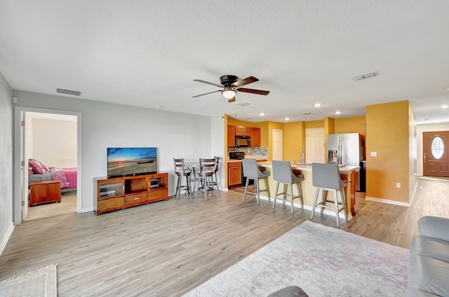 living room featuring a textured ceiling, light wood-type flooring, and ceiling fan