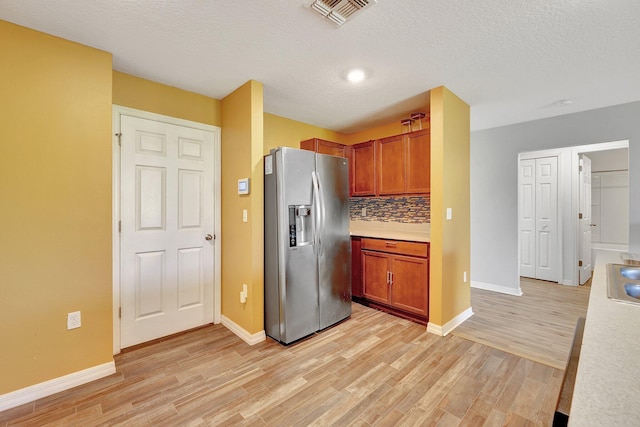 kitchen with backsplash, light hardwood / wood-style flooring, a textured ceiling, and stainless steel refrigerator with ice dispenser