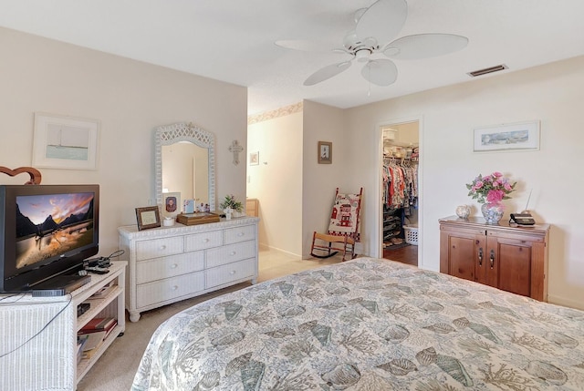 bedroom with light carpet, visible vents, a ceiling fan, a closet, and a walk in closet