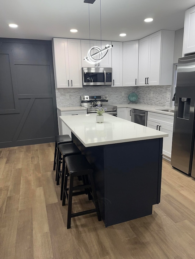 kitchen with pendant lighting, a center island, appliances with stainless steel finishes, light hardwood / wood-style floors, and white cabinetry