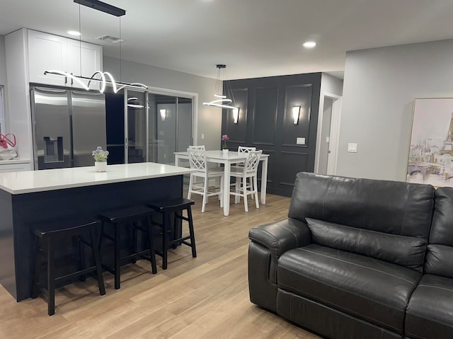 kitchen featuring decorative light fixtures, white cabinetry, light wood-type flooring, and stainless steel fridge with ice dispenser