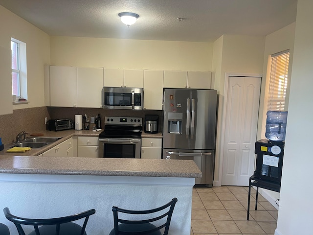 kitchen with light tile patterned floors, kitchen peninsula, sink, and appliances with stainless steel finishes