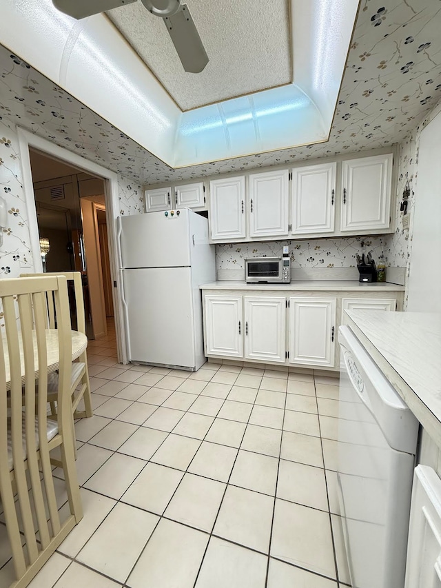 kitchen with ceiling fan, white cabinets, white appliances, a tray ceiling, and light tile patterned floors