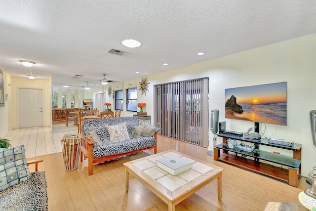 living room featuring ceiling fan, a textured ceiling, and light hardwood / wood-style flooring