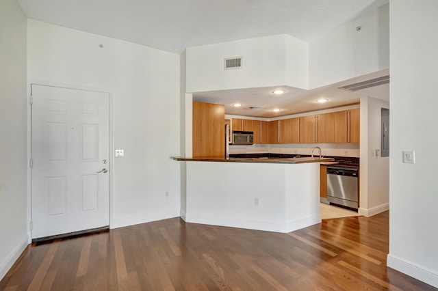 kitchen with kitchen peninsula, wood-type flooring, stainless steel appliances, and electric panel