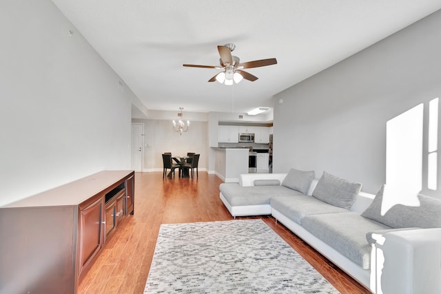 living room featuring ceiling fan with notable chandelier and light hardwood / wood-style flooring