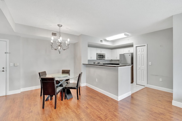 dining space featuring a textured ceiling, an inviting chandelier, and light hardwood / wood-style flooring