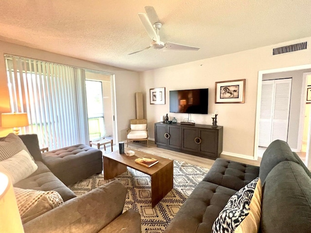 living room with ceiling fan, a textured ceiling, and light wood-type flooring