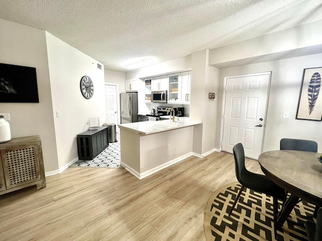 kitchen with light hardwood / wood-style flooring, kitchen peninsula, a textured ceiling, white cabinets, and appliances with stainless steel finishes