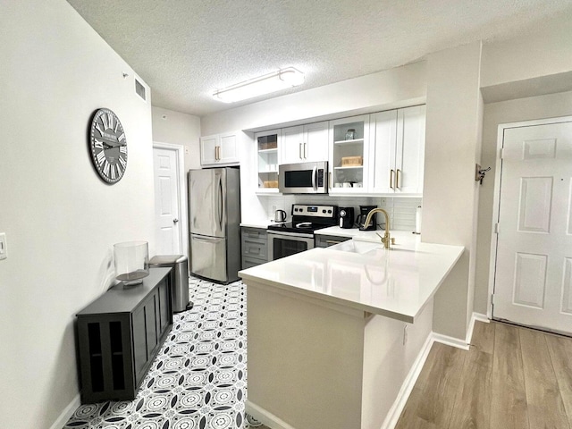 kitchen with white cabinetry, sink, stainless steel appliances, kitchen peninsula, and a textured ceiling