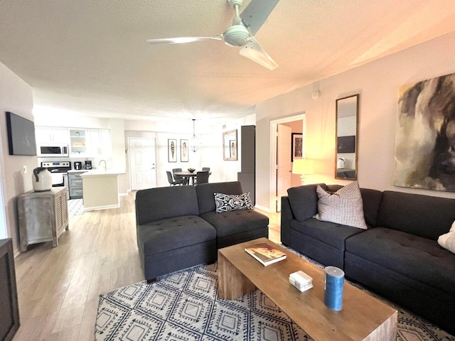 living room featuring a textured ceiling, sink, ceiling fan with notable chandelier, and light wood-type flooring