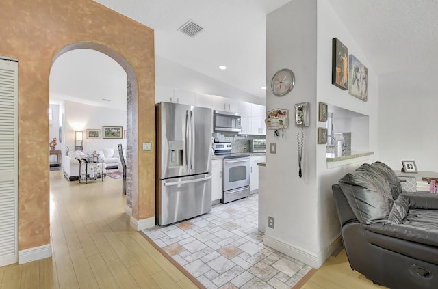 kitchen with backsplash, white cabinets, light hardwood / wood-style flooring, vaulted ceiling, and appliances with stainless steel finishes