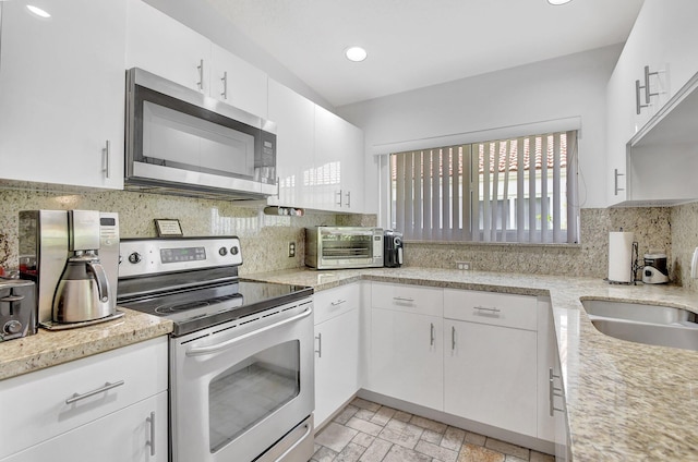 kitchen with appliances with stainless steel finishes, tasteful backsplash, light stone counters, sink, and white cabinets