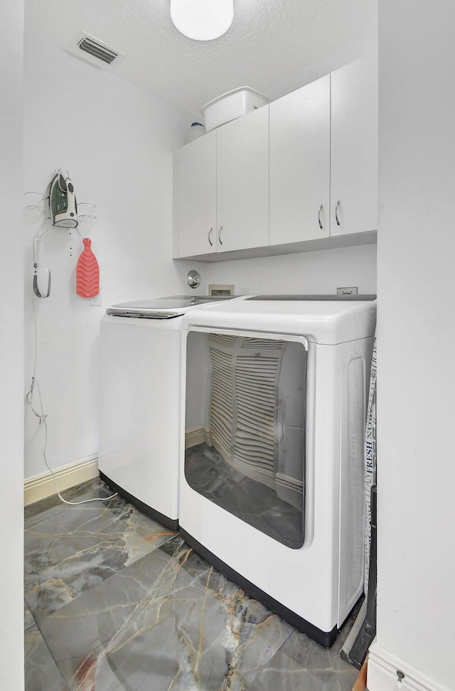 laundry area featuring washer and dryer, cabinets, and a textured ceiling