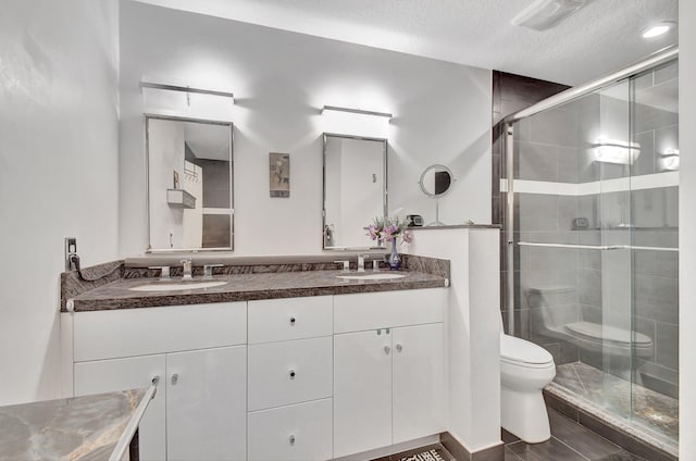 bathroom with vanity, a shower with shower door, a textured ceiling, and toilet