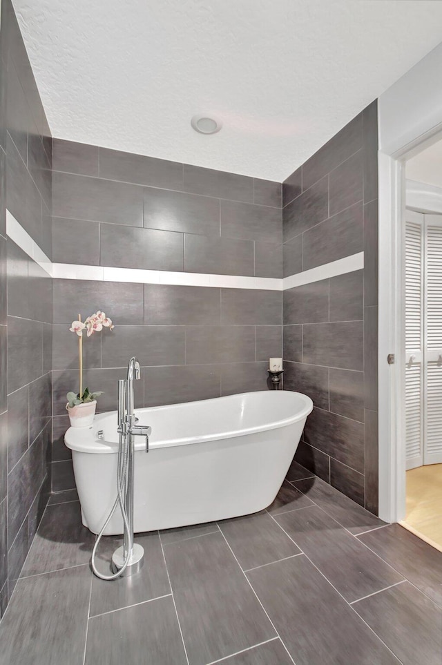 bathroom featuring a textured ceiling, a tub to relax in, tile patterned floors, and tile walls