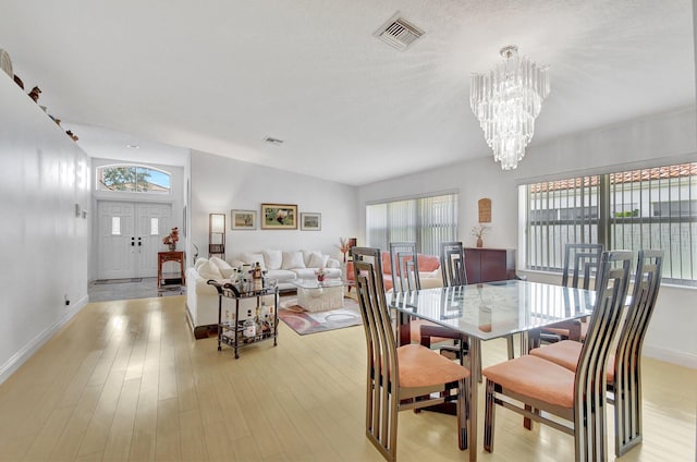 dining area featuring an inviting chandelier, vaulted ceiling, and light wood-type flooring