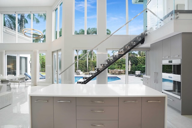 kitchen featuring gray cabinets, plenty of natural light, a towering ceiling, and stainless steel double oven