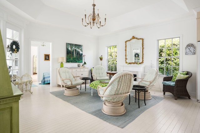 living room with ornamental molding, an inviting chandelier, a raised ceiling, and light hardwood / wood-style floors