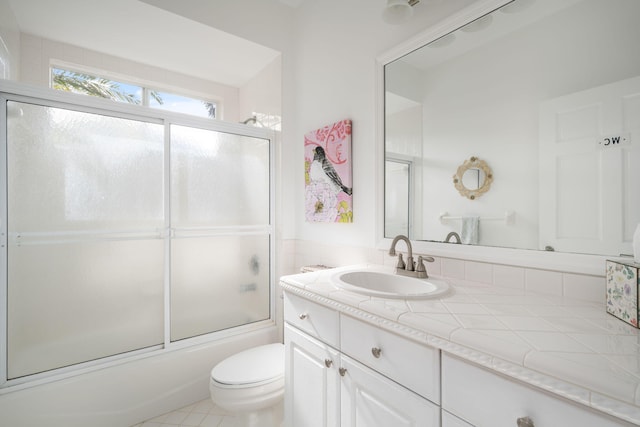 full bathroom with tile patterned flooring, vanity, bath / shower combo with glass door, and toilet