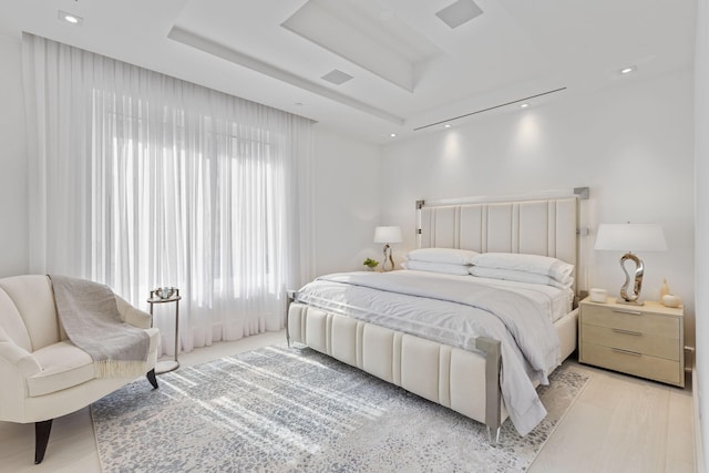 bedroom with a tray ceiling and light wood-type flooring