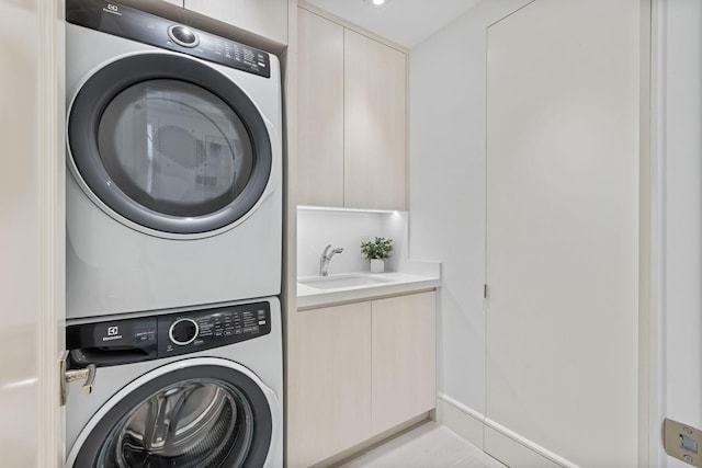 clothes washing area with cabinets, stacked washing maching and dryer, and sink