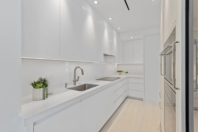 kitchen with white cabinets, black electric stovetop, sink, and light hardwood / wood-style flooring