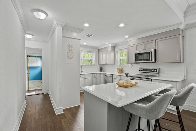 kitchen featuring appliances with stainless steel finishes, dark wood-type flooring, crown molding, gray cabinets, and a kitchen island