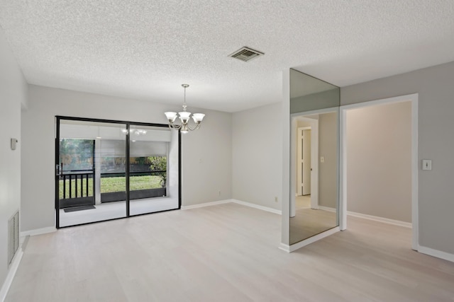 spare room featuring light hardwood / wood-style floors, a textured ceiling, and a chandelier