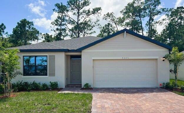 ranch-style home with stucco siding, decorative driveway, roof with shingles, a front yard, and an attached garage