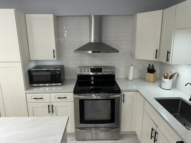 kitchen with sink, appliances with stainless steel finishes, white cabinetry, light stone counters, and wall chimney exhaust hood