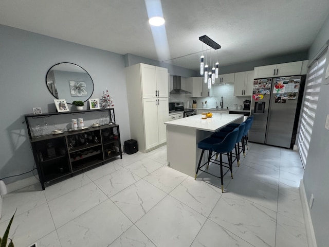 kitchen featuring pendant lighting, wall chimney range hood, sink, appliances with stainless steel finishes, and a kitchen island