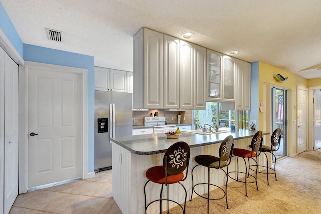 kitchen with sink, stainless steel fridge, light tile patterned flooring, kitchen peninsula, and a breakfast bar area