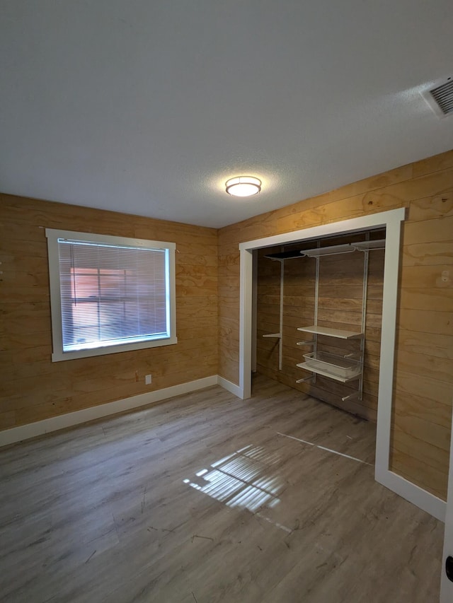 unfurnished bedroom with wood walls, wood-type flooring, a textured ceiling, and a closet