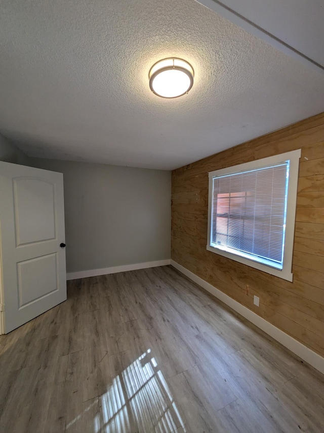 bonus room with wood walls, light hardwood / wood-style floors, and a textured ceiling