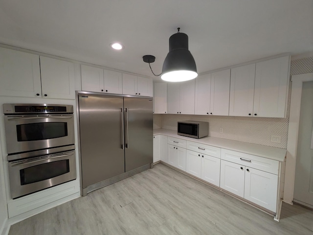 kitchen featuring decorative backsplash, appliances with stainless steel finishes, light hardwood / wood-style flooring, white cabinetry, and hanging light fixtures