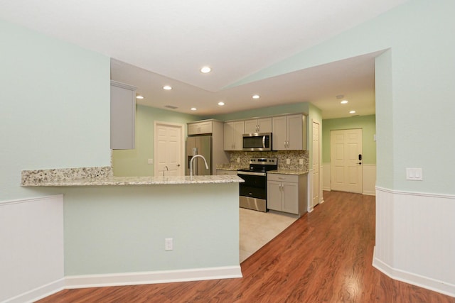 kitchen with backsplash, light stone countertops, appliances with stainless steel finishes, light hardwood / wood-style floors, and kitchen peninsula