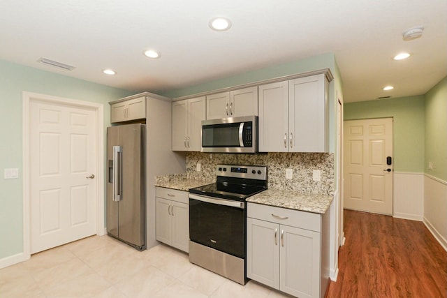 kitchen featuring light stone counters, light wood-type flooring, appliances with stainless steel finishes, and tasteful backsplash