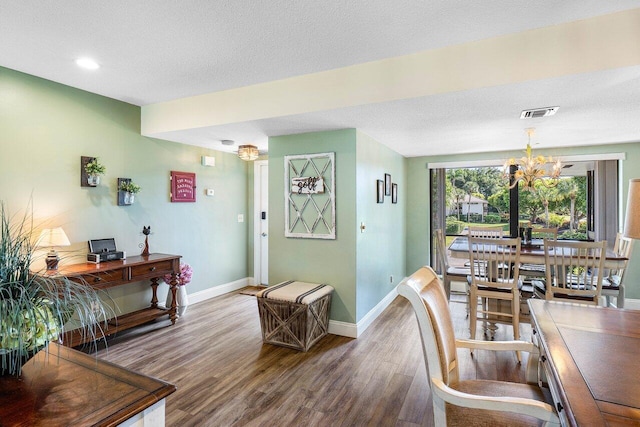 dining area with wood-type flooring, a textured ceiling, and a notable chandelier