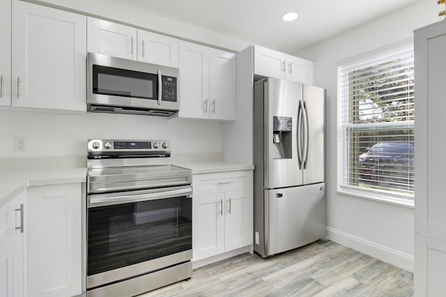 kitchen with white cabinets, light wood-type flooring, and stainless steel appliances