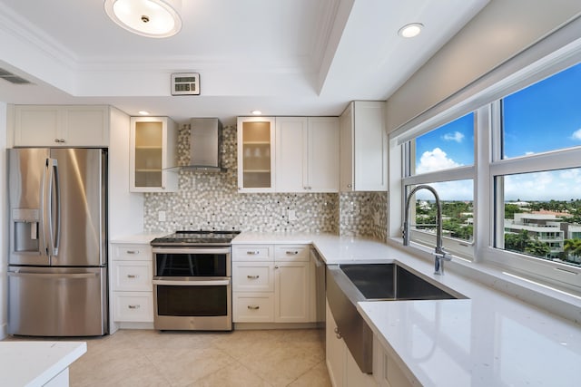 kitchen with backsplash, stainless steel appliances, a raised ceiling, crown molding, and wall chimney range hood