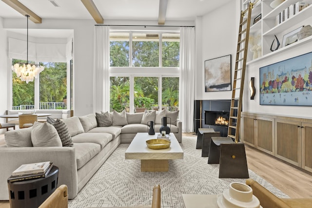 living room featuring an inviting chandelier, a tiled fireplace, light hardwood / wood-style flooring, and beamed ceiling