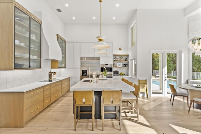 kitchen featuring white cabinetry, hanging light fixtures, a center island with sink, black electric cooktop, and stainless steel built in fridge